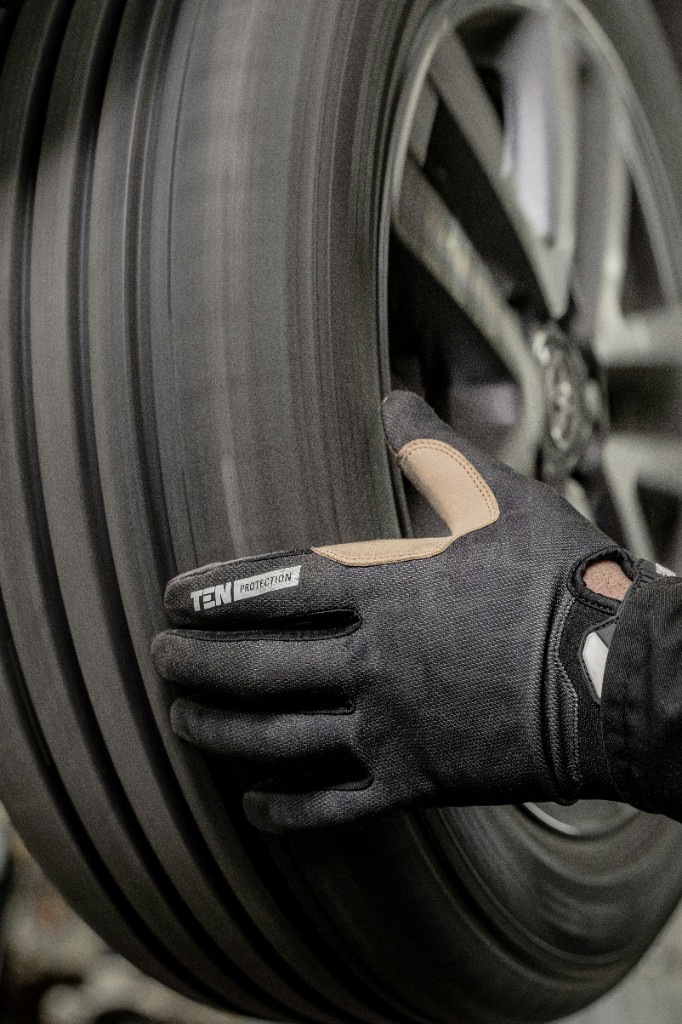 Technicien avec gant de protection touchant un pneu en rotation — balancement ou inspection en atelier